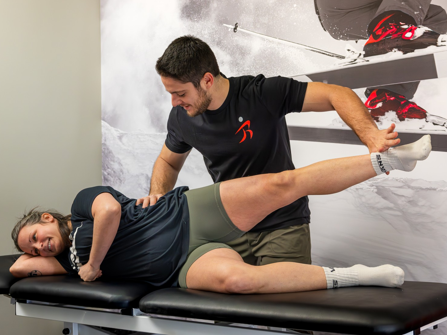 Physical therapist assisting a patient with a side-lying leg stretch on a treatment table.