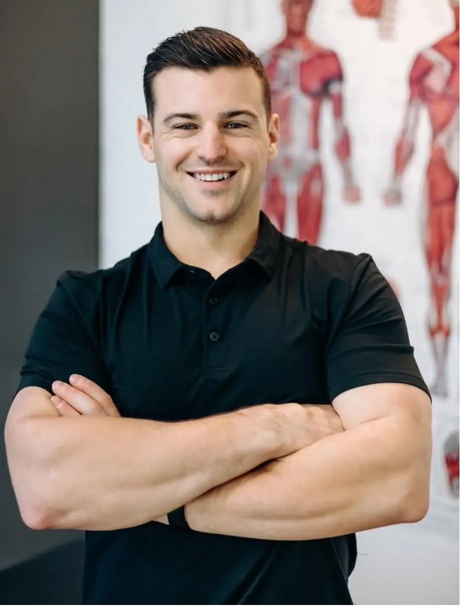 "Smiling osteopath standing with arms crossed in a rehabilitation clinic."
